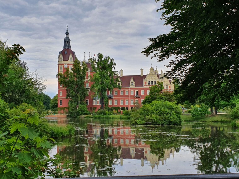 Blick auf das Muskauer Schloss und den Park. Das Schloss spiegelt sich im Wasser von einem See.